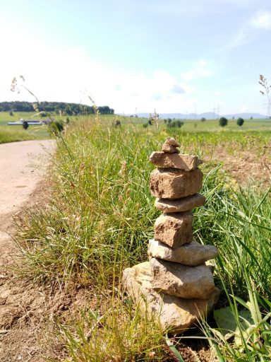 Balance Steinerne Turm aus mehreren Steinen entlang eines Feldwegs, umgeben von Gras.